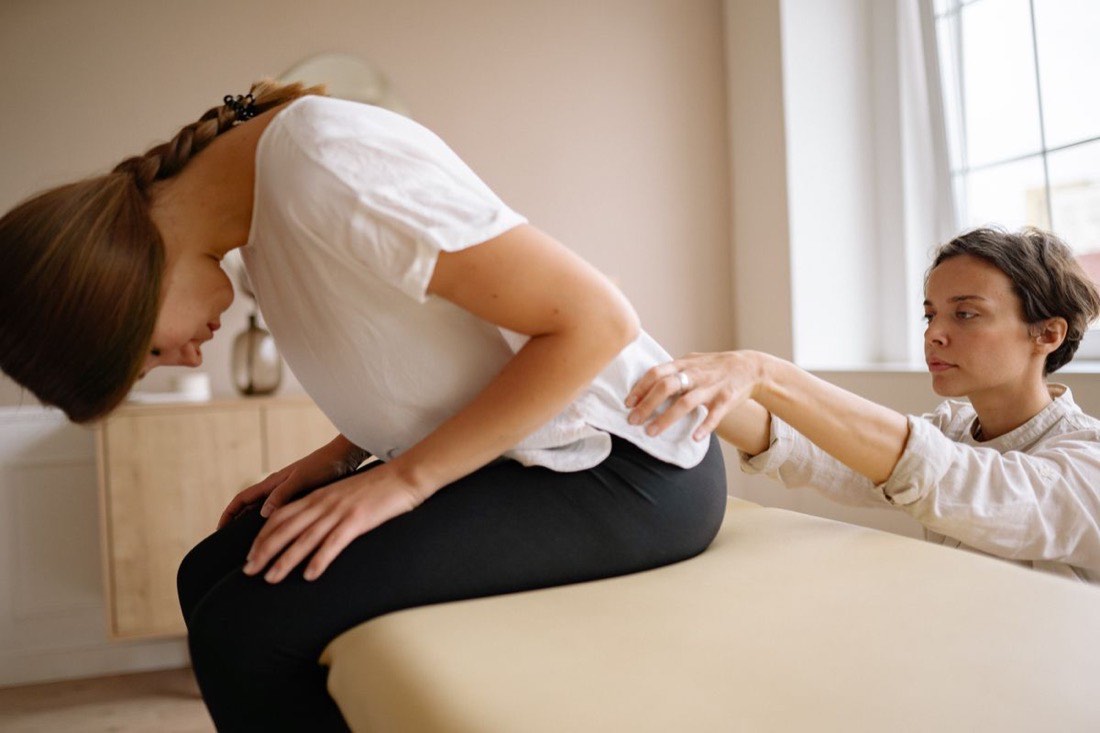 Physiotherapeutin untersucht den Rücken einer Patientin auf der Behandlungsliege